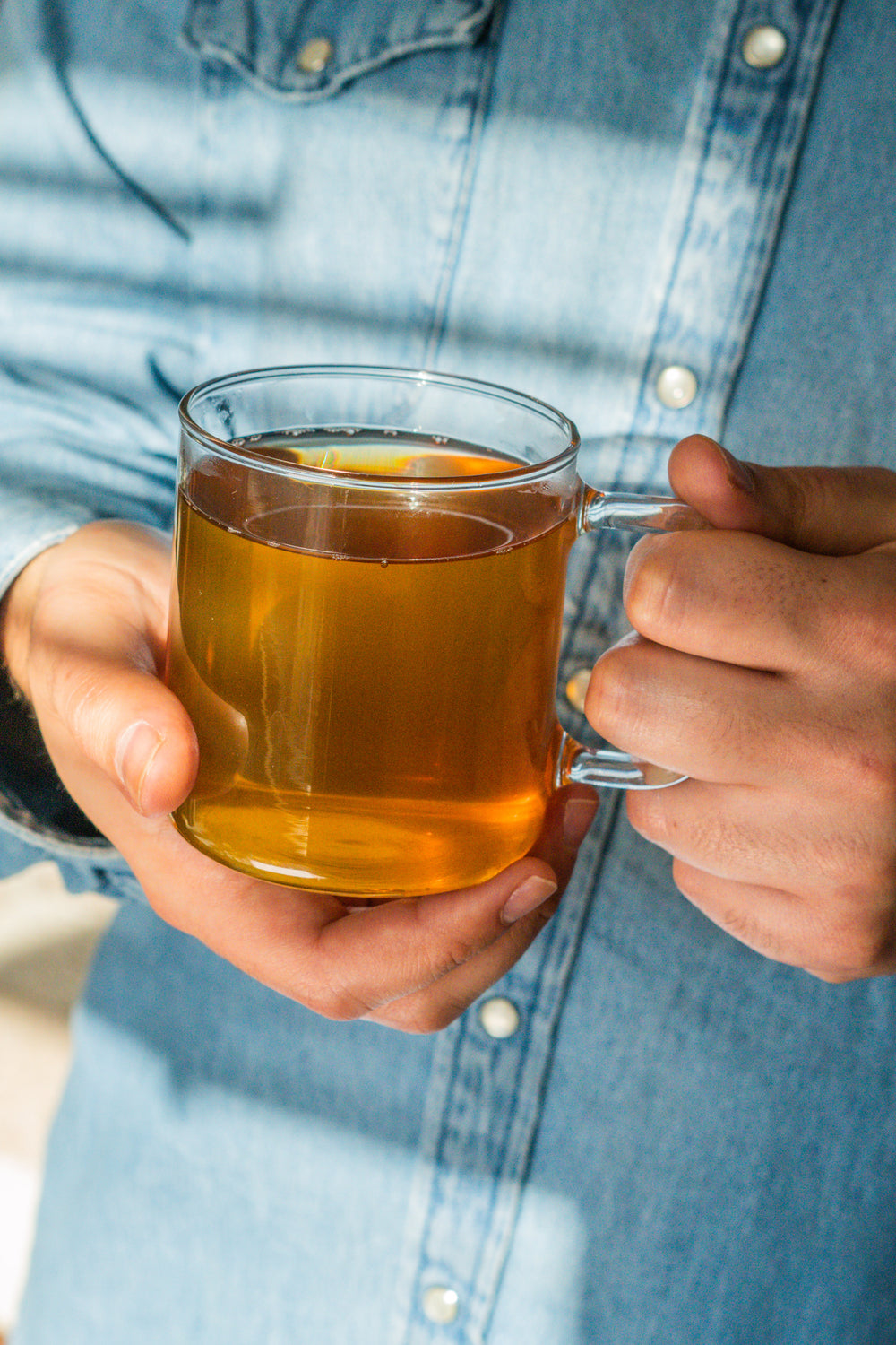 Person holding a mug of tea with a blue denim shirt background